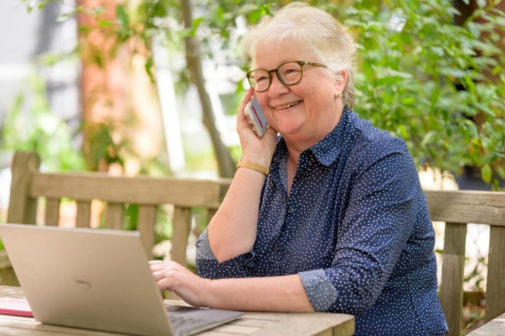 An older adult is using her laptop and calling the Social Security office to check her SSDI claim status.